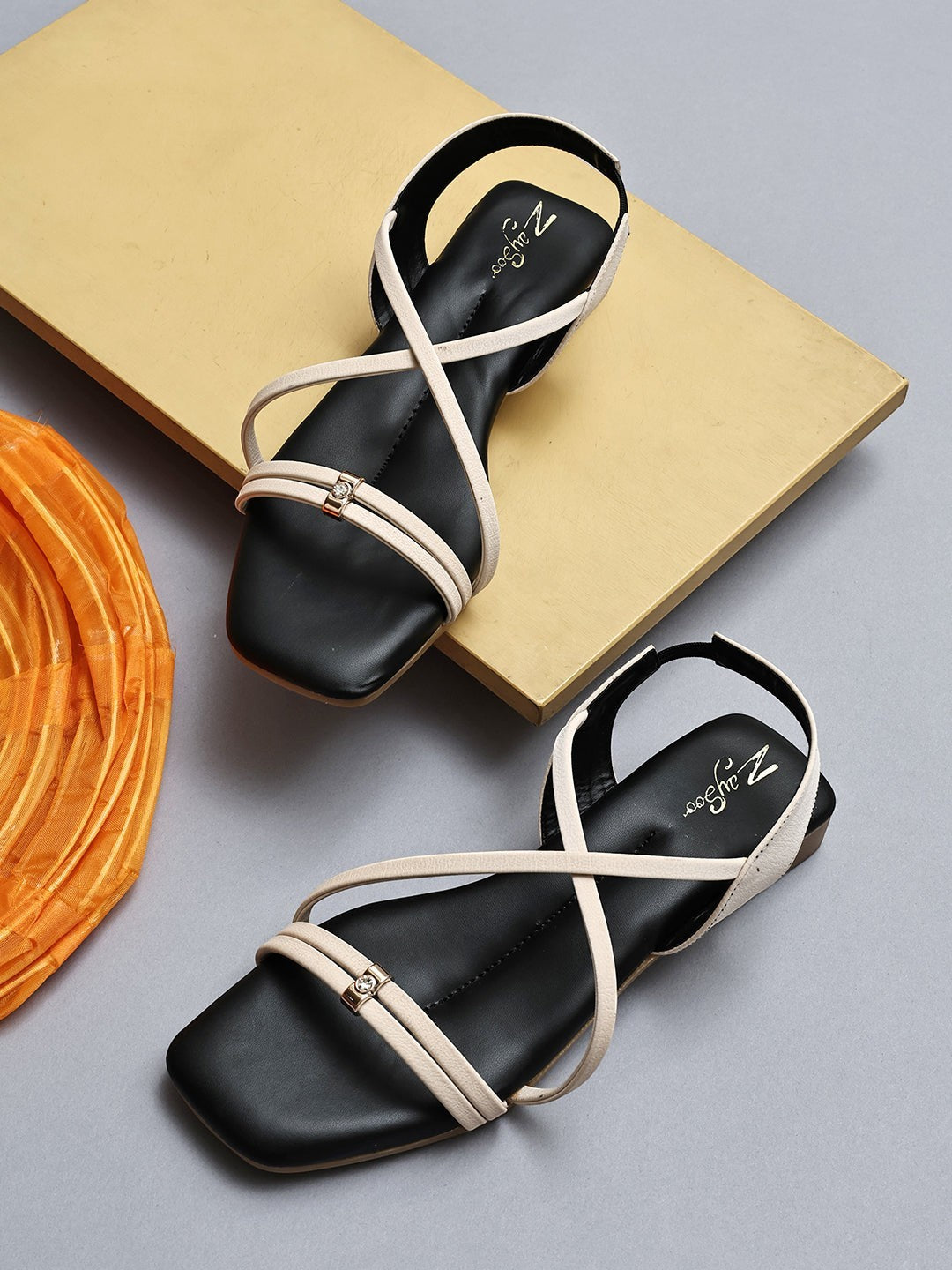 Zaysoo women's black flat sandals with beige criss-cross straps and a back strap, featuring a small metallic ornament.